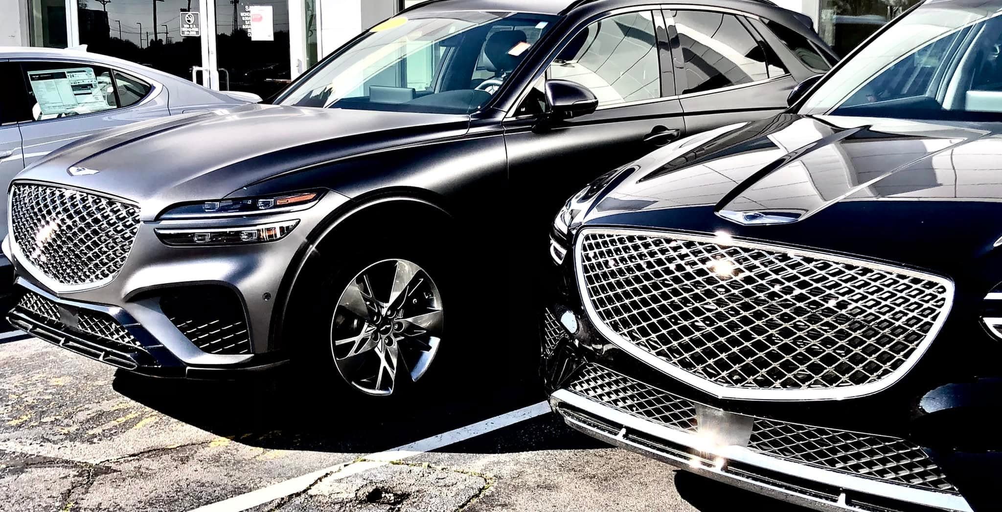 Matte grey and glossy black Genesis SUVs parked side-by-side, highlighting their large diamond-patterned grilles.